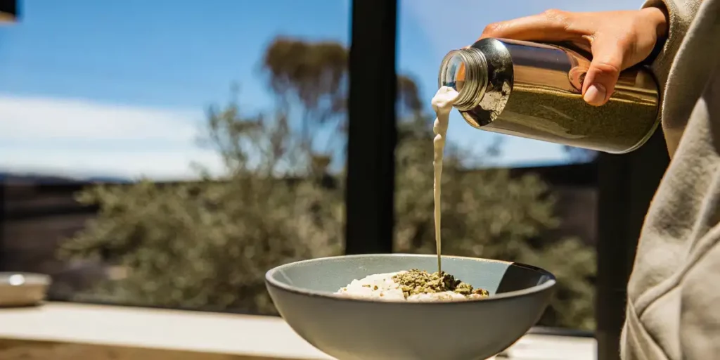 Pouring cannabis-infused milk onto a breakfast bowl filled with oats and ground cannabis