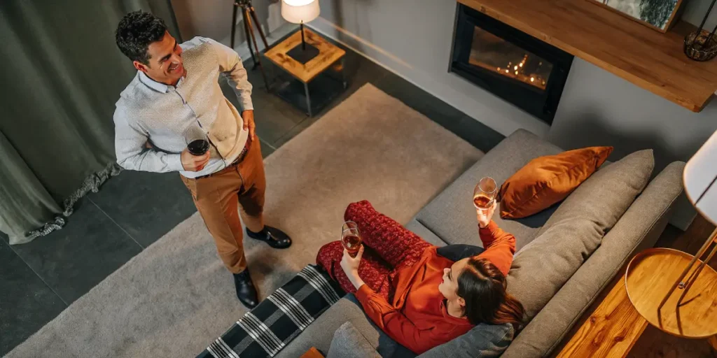 Overhead view: a couple enjoying drinks in a sophisticated living room with a fireplace, during a house party.