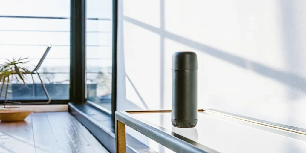 Matte black spray can shaped container resting on a glass table in a modern, sunlit room.