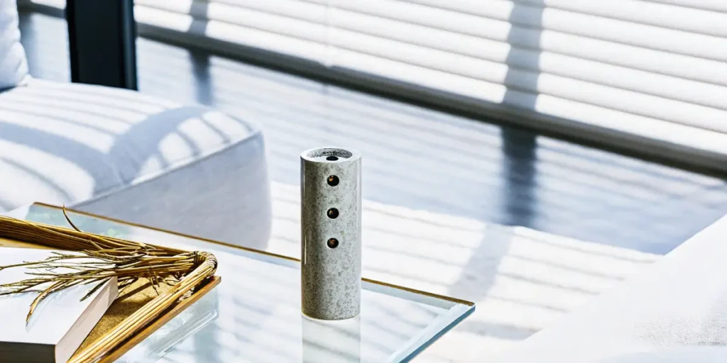 Polished stone 3-hole hash pipe resting on a glass coffee table next to a decorative tray in a bright living room.