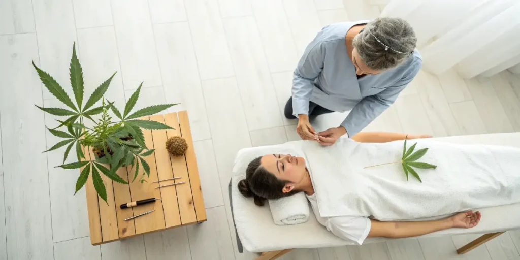 Wellness therapist performing acupuncture on a patient with cannabis leaves nearby.